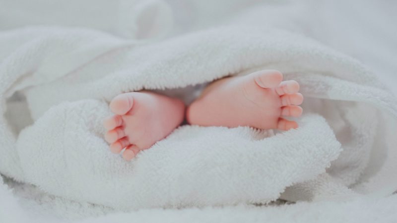 barefooted baby covering white blanket